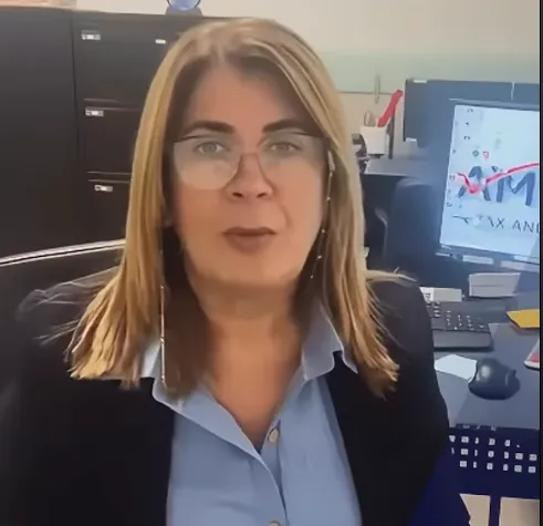 Image of woman speaking into camera. There's an IRS logo on the foreground. The woman is wearing a black business suit and white collar shirt. There's a computer with the America Tax & Accounting, Corp. Logo in the background.